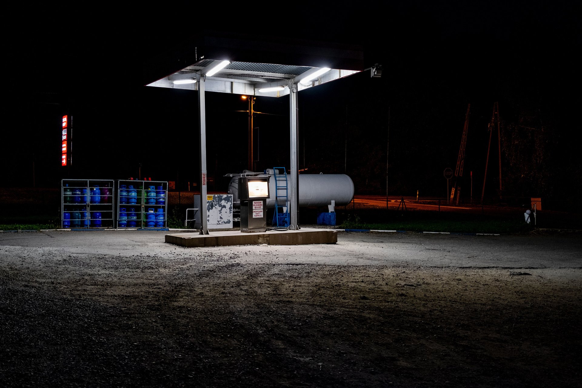 Gasolinera solitaria iluminada de noche, canopy industrial, sin vehículos ni gente — atmosfera cinematográfica que evoca el drive-off nocturno