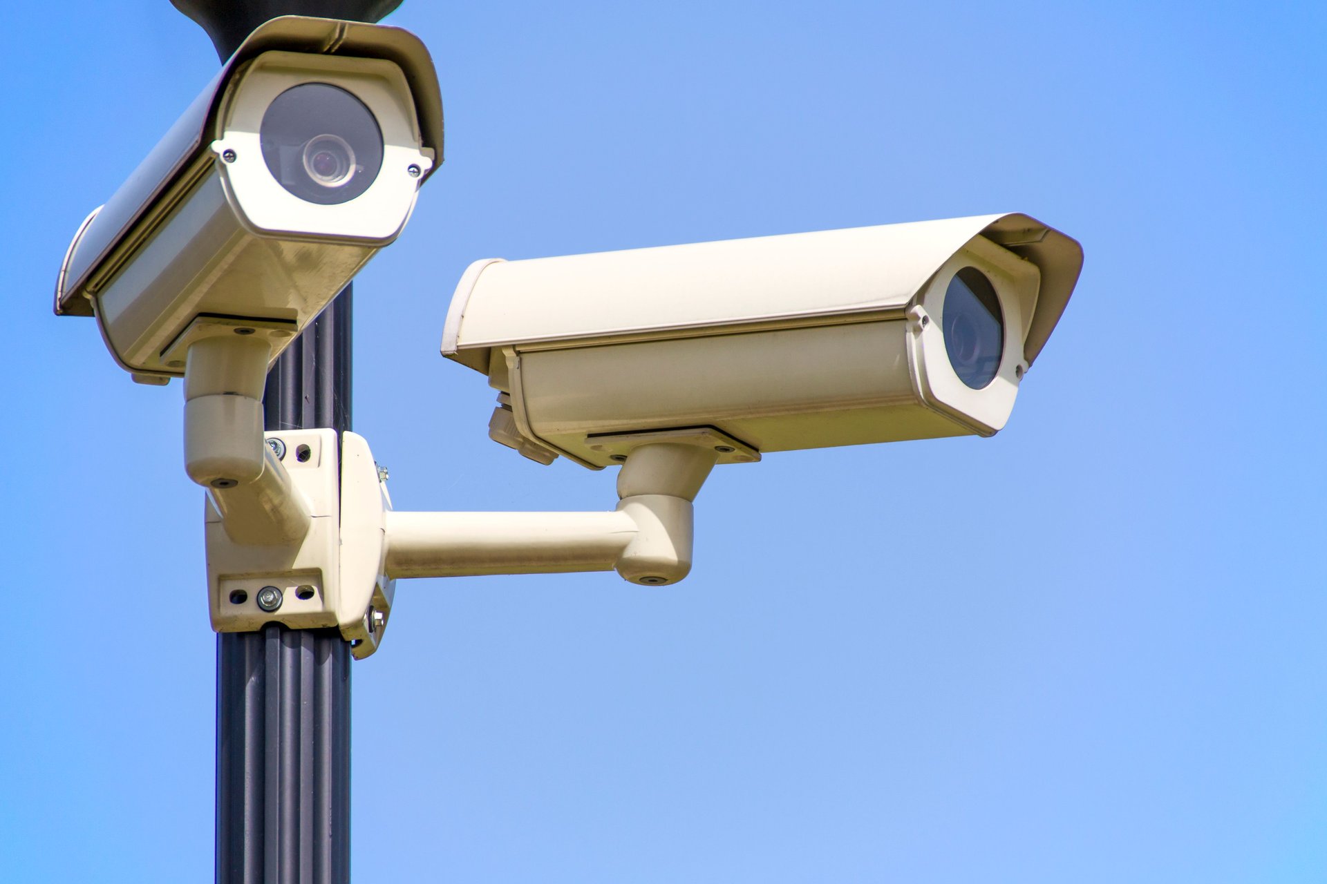 Dos cámaras CCTV de exterior tipo bullet montadas en poste metálico contra cielo azul — instalación profesional de vigilancia sin marca visible del fabricante