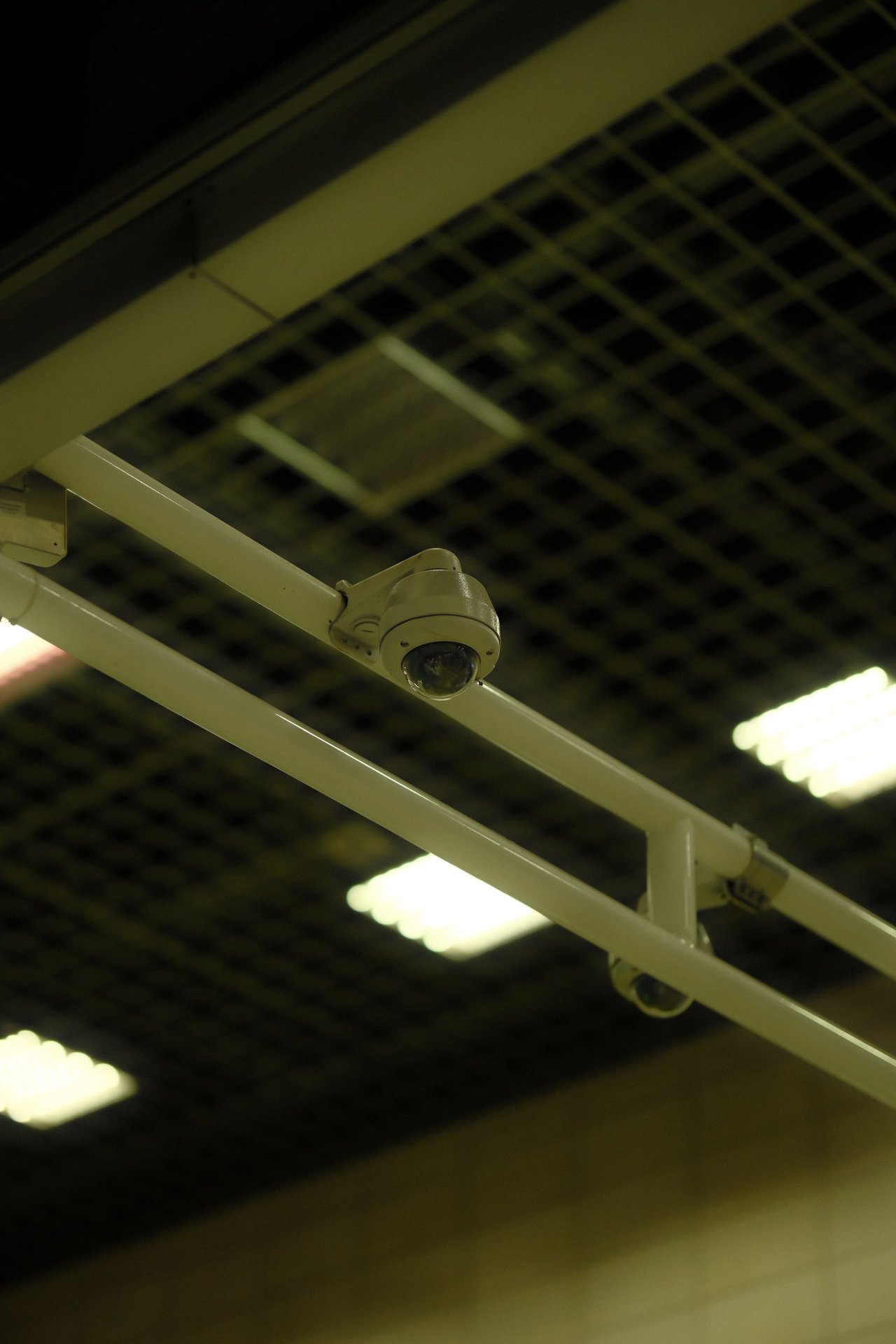 Cámara dome CCTV montada en techo industrial sobre pasillo comercial, ángulo cenital de vigilancia retail