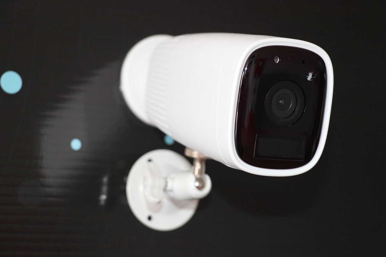 Cámara de CCTV de seguridad genérica en formato bullet blanco montada sobre fondo oscuro desenfocado, sin logos de vendor, sin texto visible.