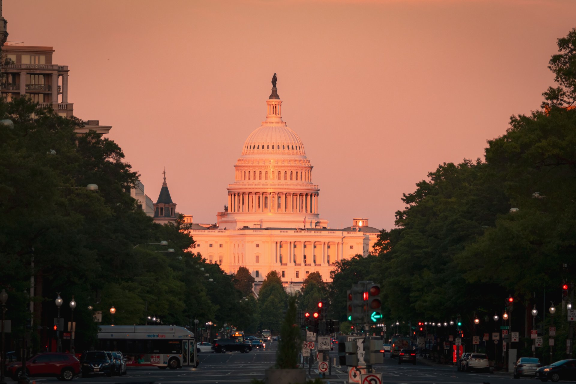 Fachada del Capitolio de EE.UU. al atardecer, vista desde Pennsylvania Avenue con la cúpula iluminada sobre cielo rosa