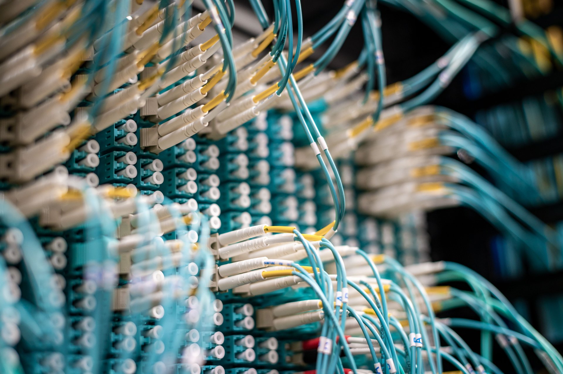 Pasillo oscuro de centro de datos con bandejas de cables de red — la cadena invisible detras de cada entrega de datos