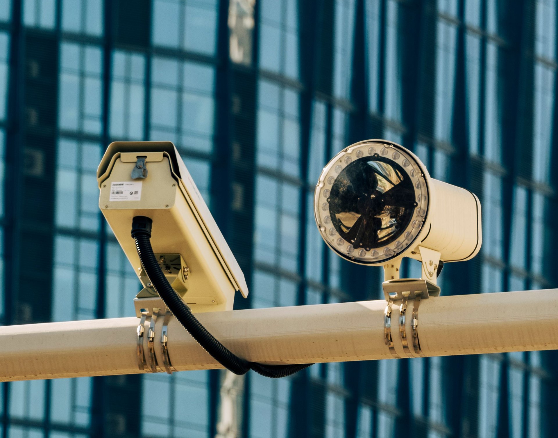 Dos cámaras de vigilancia montadas en un poste urbano frente a un edificio de cristal